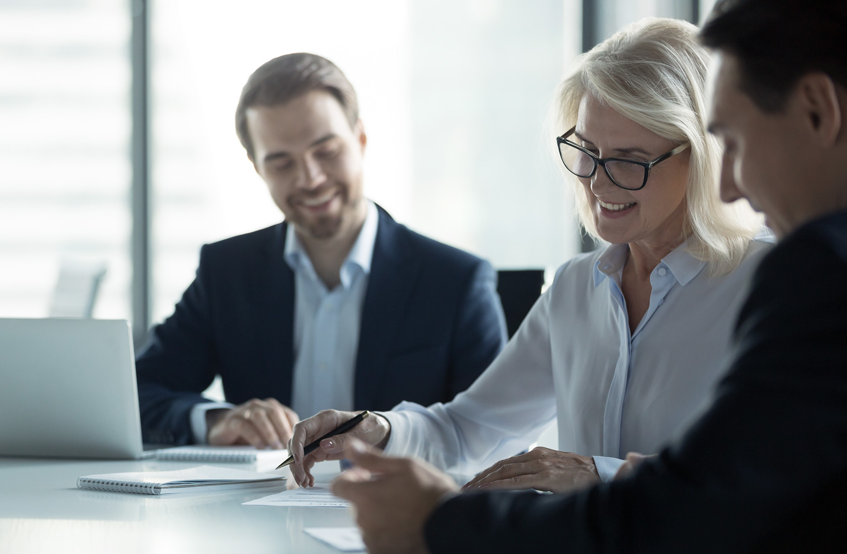 Business woman signs a document at a meeting table with two business men