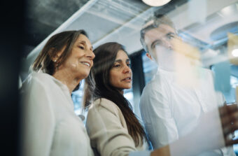 Two mature business women and a male colleague discuss post it notes on a glass panel