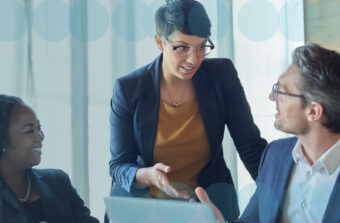 Three colleagues in discussion at a meeting table in a brightly lit room