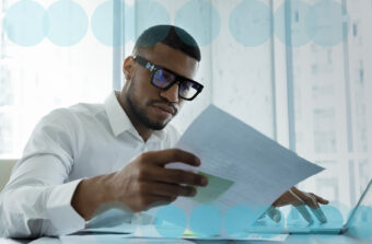 Business man using a laptop and looking at a piece of paper to review compliance processes