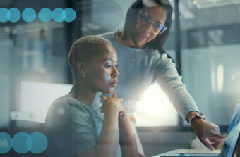 Two female collegues work at computer monitor in a dramatically lit modern office space