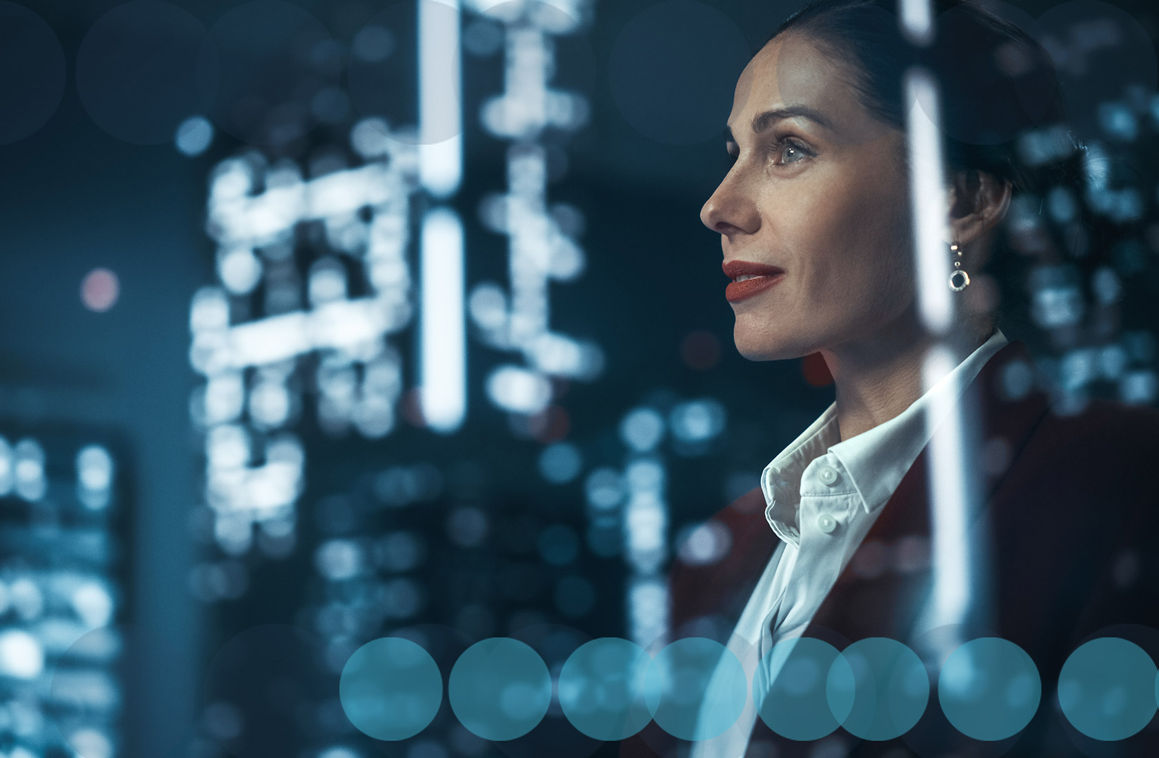 A medium close up profile shot of a business woman wearing a white shirt and dark jacket. She's staring off to the left. It is shot through glass, whoing the relfection of building lights in front of her